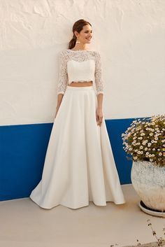 a woman standing next to a flower pot wearing a white wedding dress and crop top