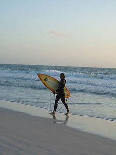 a person walking on the beach with a surfboard in their hand and water behind them