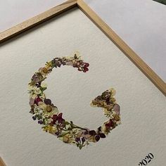 the letter c is made up of flowers and leaves on white paper with a wooden frame