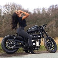 a woman sitting on top of a motorcycle next to a road with trees in the background