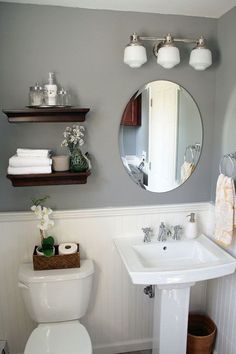 a white toilet sitting next to a sink in a bathroom under a mirror and shelves