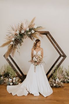 a woman standing in front of a wooden frame with flowers and greenery on it