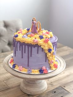 there is a purple cake with yellow icing on the top and flowers around it