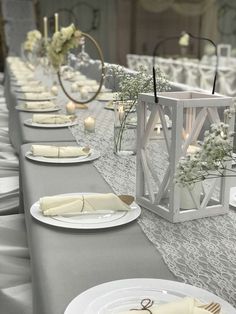 a long table set with white plates and silver napkins for an elegant wedding reception