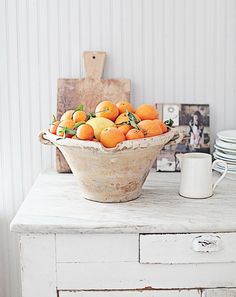 a wooden bowl filled with oranges sitting on top of a white dresser next to plates