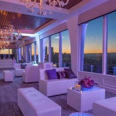 a room filled with lots of white furniture next to tall windows at sunset or dawn