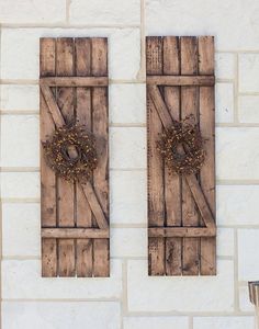 two wooden doors with wreaths on them against a white brick wall