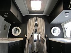 the inside of a motor home with curtains and sink area in front of it, along with two round windows