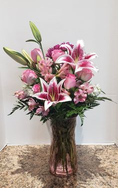 a vase filled with pink and white flowers on top of a marble counter next to a wall