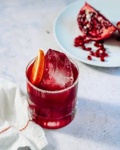 a red drink sitting on top of a table next to a slice of pomegranate