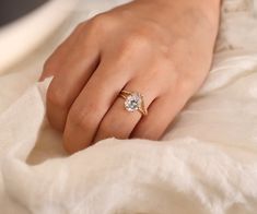 a woman's hand with a diamond ring on her finger, sitting on a white blanket