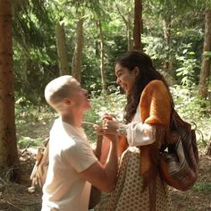 two people standing in the woods talking to each other