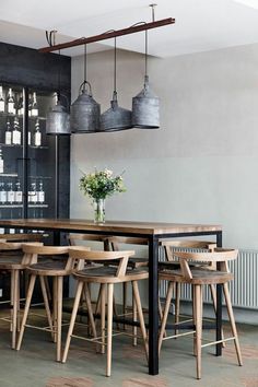 a dining room table with chairs and stools in front of an open shelf filled with bottles