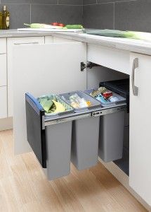 an open trash can in the middle of a kitchen with white cupboards and drawers