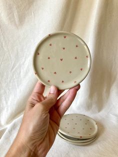 a person holding two plates in their hand on a white cloth covered surface with red hearts