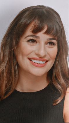 a close up of a person wearing a black dress and smiling at the camera with long hair