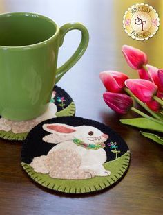 two coasters on a table with pink tulips and a green coffee cup