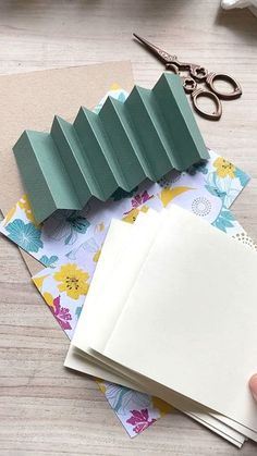 someone is cutting out paper with scissors on top of the papers and other crafting supplies