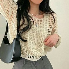 a woman with long black hair wearing a white shirt and grey pants holding a gray purse