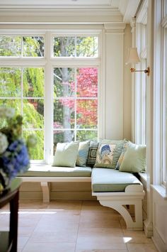 a window seat with pillows and flowers in front of it