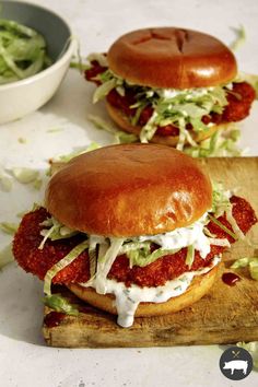 two burgers with lettuce and tomato on a cutting board