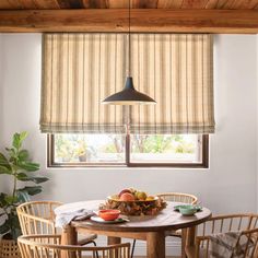 a dining room table with chairs and a bowl of fruit on it in front of a window