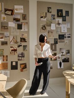 a woman standing in front of a wall with many pictures on it and holding a book