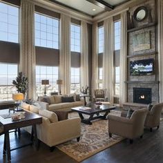 a living room filled with lots of furniture and large windows covered in shades of brown