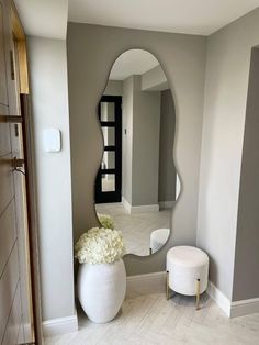 a white vase with flowers in it sitting next to a large mirror on the wall