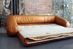 a brown leather couch sitting on top of a gray floor next to a brick wall