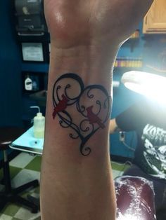 a heart shaped tattoo with two birds on it's wrist, in the middle of a room