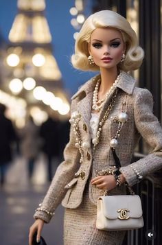 a barbie doll dressed in a tweed suit and pearls holding a white purse with the eiffel tower in the background