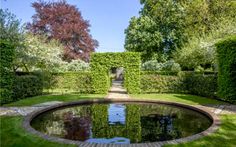 a pond surrounded by hedges in the middle of a garden