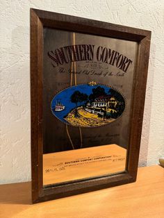 the southern comfort sign is displayed in a wooden frame on top of a table next to a wall