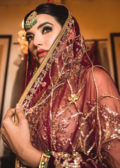 a woman in a red and gold bridal outfit with her veil draped over her head