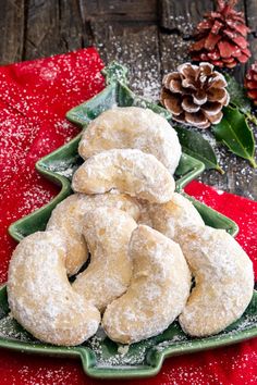 powdered sugar covered doughnuts on a green platter with pine cones in the background