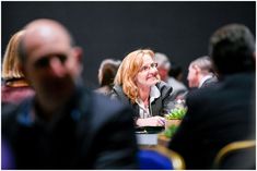 a woman sitting at a table with other people around her and smiling for the camera