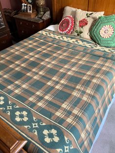 a bed with plaid bedspread and pillows on it in a room filled with wooden furniture