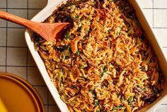 a casserole dish with rice and vegetables in it next to a wooden spoon