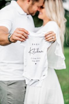 a man and woman holding up a white shirt that says, baby nathan coming home