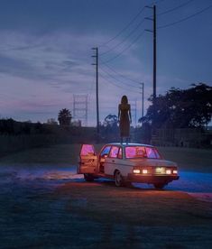 a woman standing on top of a car in the middle of a field at night