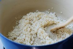 rice being cooked in a blue pot with a wooden spoon