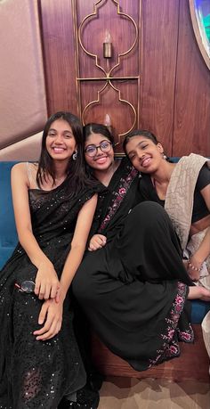 three women sitting on a blue couch posing for the camera with their arms around each other