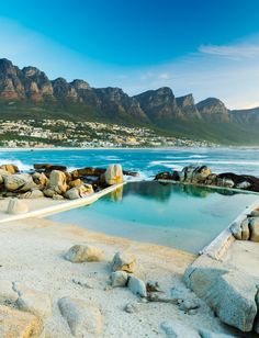 an outdoor swimming pool surrounded by rocks and water with mountains in the backgroud