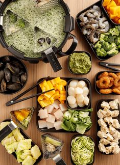 many different types of food in trays on a wooden table with utensils