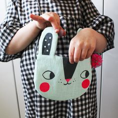 a person holding a small bag with a cat design on it's side and pointing at the camera