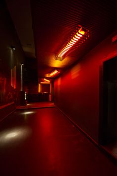 an empty hallway with red light coming from the ceiling and lights shining down on the floor