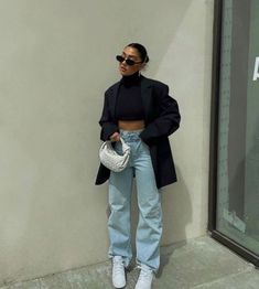 a woman standing in front of a building wearing high waist jeans and black blazer