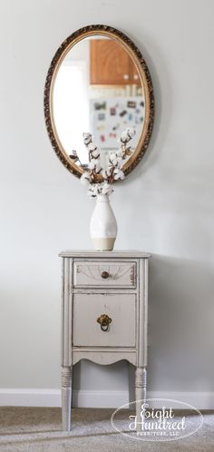 a small white table with a mirror on top of it and flowers in a vase