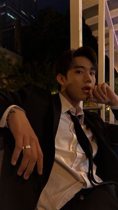 a young man in a suit and tie sitting on a chair with his hand near his mouth